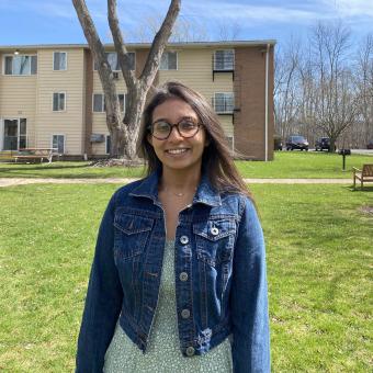 Prachi Shah wears a denim jacket and stands in front of an apartment building